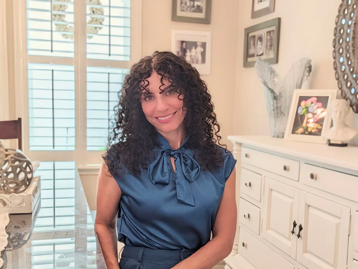 Leah Klein smiling in a navy blue blouse in her sunlit home.